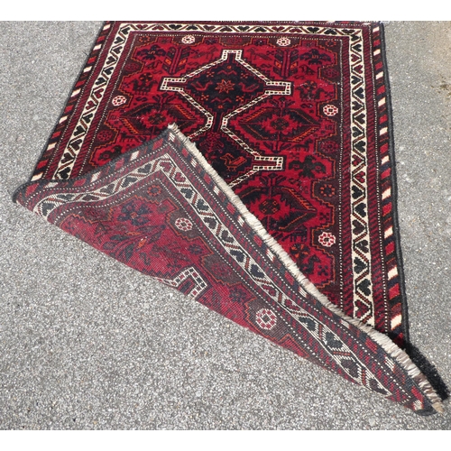 21 - A Persian rug, decorated with three central diamond shaped motifs, bordered by repeating designs, on... 