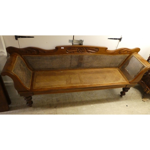 24 - A modern Colonial design fruitwood framed, scroll end settee with a caned back and seat, raised on t... 