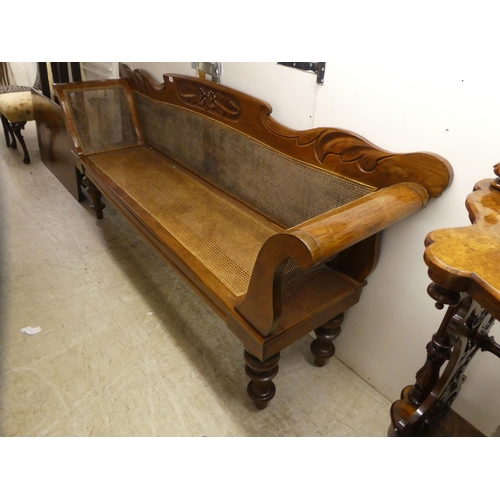 24 - A modern Colonial design fruitwood framed, scroll end settee with a caned back and seat, raised on t... 