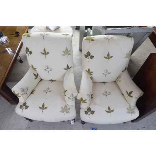 25 - A pair of late Victorian easy chairs, each upholstered in cream leaf design fabric, raised on turned... 