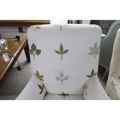 25 - A pair of late Victorian easy chairs, each upholstered in cream leaf design fabric, raised on turned... 