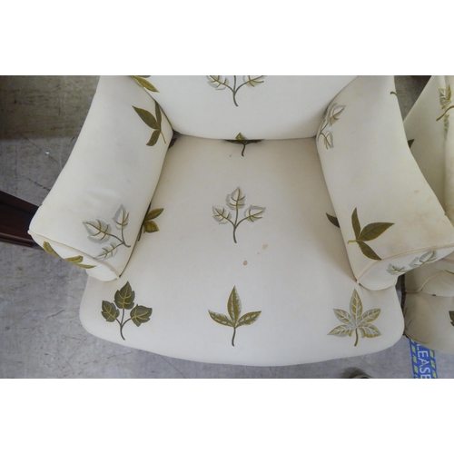 25 - A pair of late Victorian easy chairs, each upholstered in cream leaf design fabric, raised on turned... 