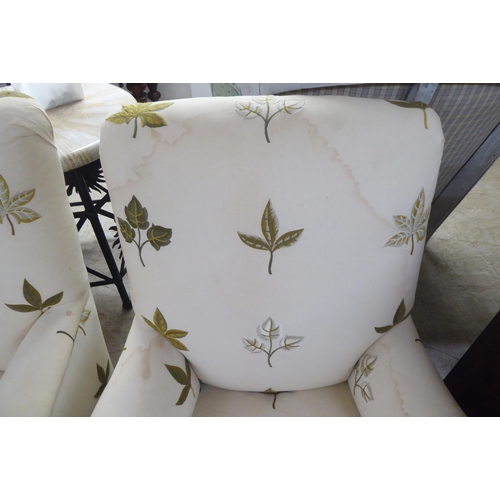 25 - A pair of late Victorian easy chairs, each upholstered in cream leaf design fabric, raised on turned... 