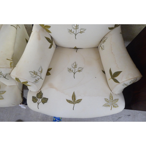 25 - A pair of late Victorian easy chairs, each upholstered in cream leaf design fabric, raised on turned... 