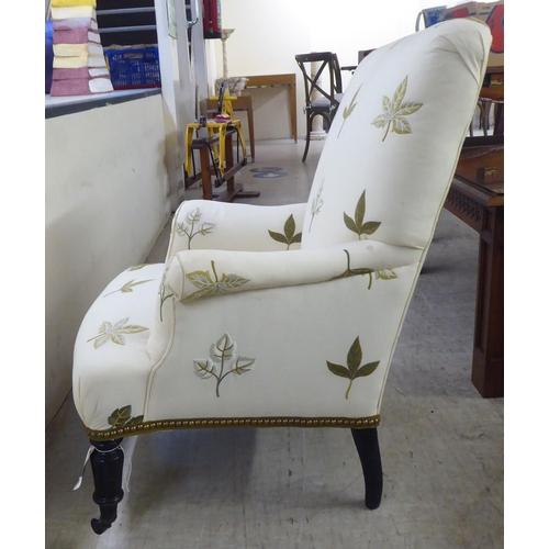 25 - A pair of late Victorian easy chairs, each upholstered in cream leaf design fabric, raised on turned... 