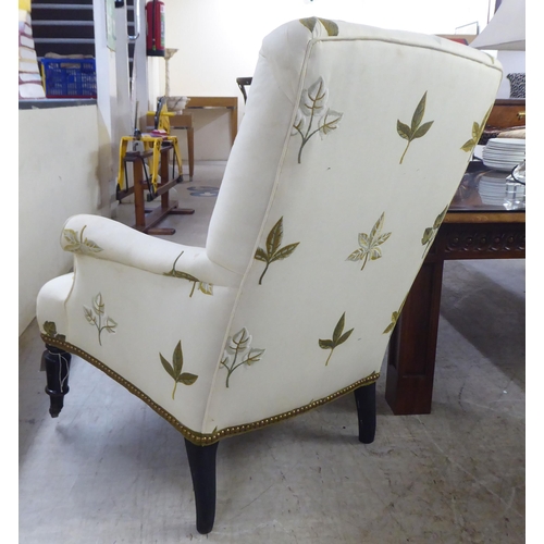 25 - A pair of late Victorian easy chairs, each upholstered in cream leaf design fabric, raised on turned... 