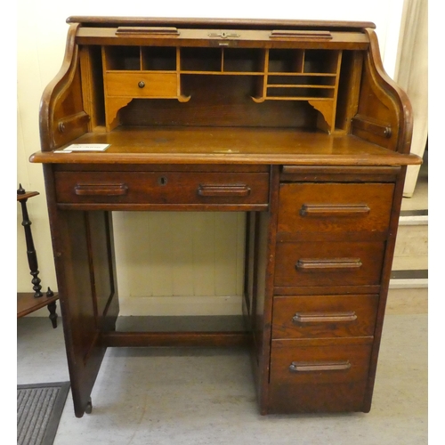 84 - An Edwardian oak roll top desk with a part-fitted pigeon hole style interior, over a single drawer a... 