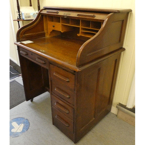 84 - An Edwardian oak roll top desk with a part-fitted pigeon hole style interior, over a single drawer a... 