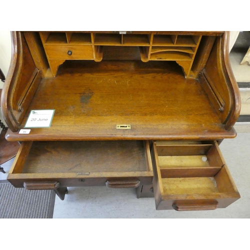 84 - An Edwardian oak roll top desk with a part-fitted pigeon hole style interior, over a single drawer a... 
