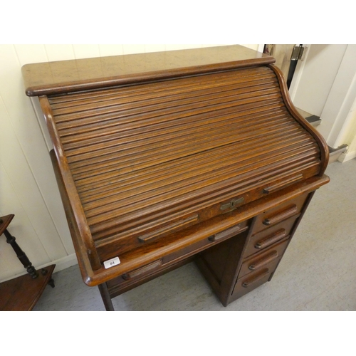 84 - An Edwardian oak roll top desk with a part-fitted pigeon hole style interior, over a single drawer a... 