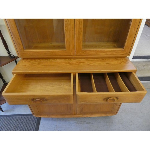 43 - An Ercol blond elm two-part cabinet, the upper section with two glazed doors, enclosing two height a... 