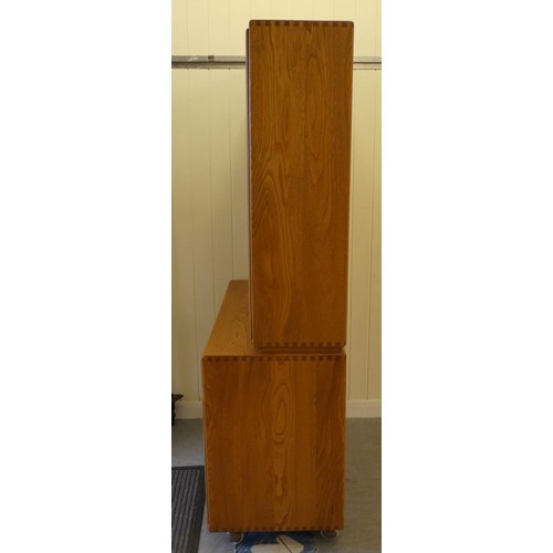 43 - An Ercol blond elm two-part cabinet, the upper section with two glazed doors, enclosing two height a... 