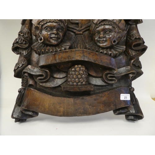 23 - An ornately carved and stained wooden wall plaque, featuring a pair of native busts, wearing identic... 