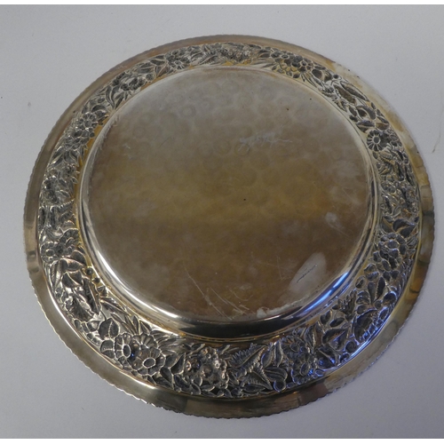 24 - A silver coloured metal charger with a dished centre within a wide, elaborately cast and chased foli... 