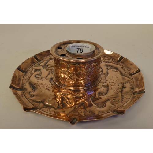 75 - An Arts & Crafts copper inkwell, the drum shape reservoir with pen holders, set on a crimped, em... 