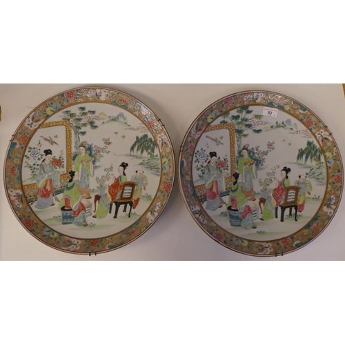 82 - A pair of late 19thC Chinese porcelain chargers, decorated in colours with figures on a veranda ... 