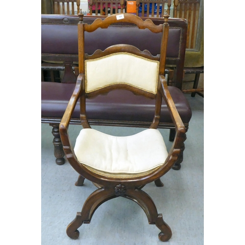 354 - An early 20thC Savonarola inspired, mahogany framed chair with a ladder back and open arms, upholste... 