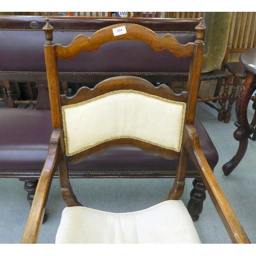 354 - An early 20thC Savonarola inspired, mahogany framed chair with a ladder back and open arms, upholste... 