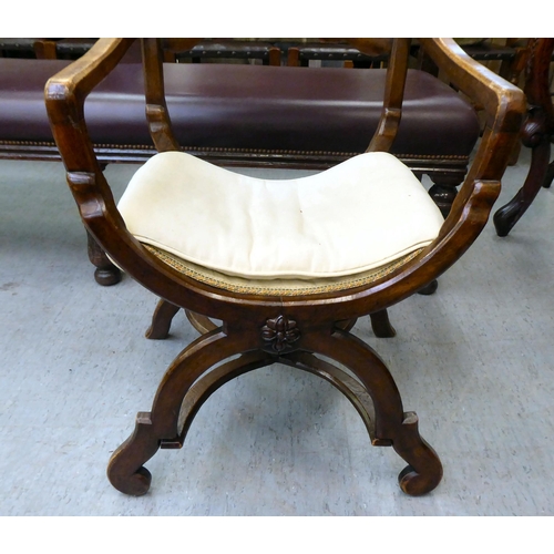 354 - An early 20thC Savonarola inspired, mahogany framed chair with a ladder back and open arms, upholste... 