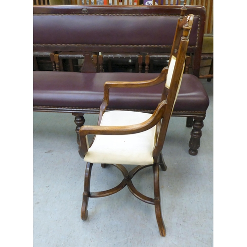 354 - An early 20thC Savonarola inspired, mahogany framed chair with a ladder back and open arms, upholste... 