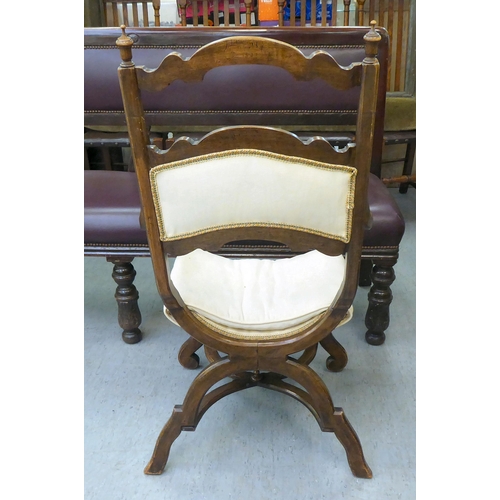 354 - An early 20thC Savonarola inspired, mahogany framed chair with a ladder back and open arms, upholste... 