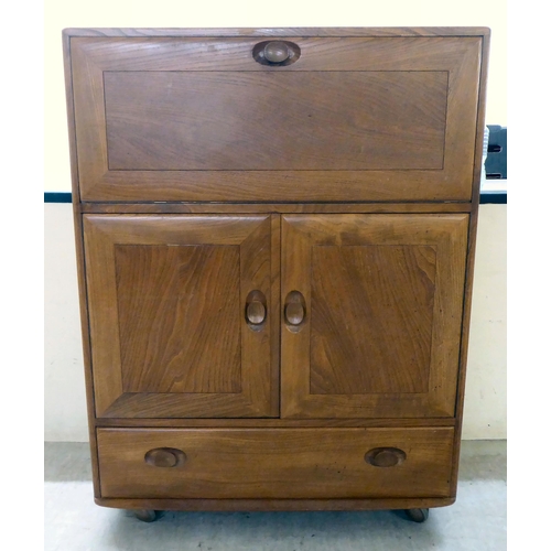 74 - An Ercol elm cocktail cabinet, the fall front over two doors and a long drawer, on a plinth and cast... 