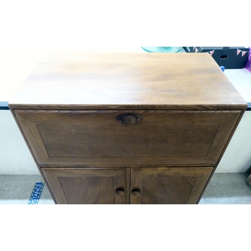 74 - An Ercol elm cocktail cabinet, the fall front over two doors and a long drawer, on a plinth and cast... 