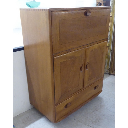 74 - An Ercol elm cocktail cabinet, the fall front over two doors and a long drawer, on a plinth and cast... 