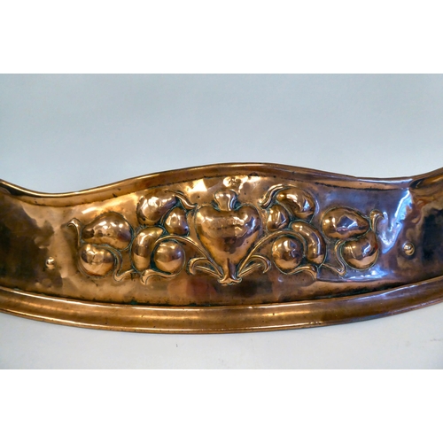 116 - An Arts & Crafts copper fire curb of curved form, embossed with soft fruit, around a central hea... 