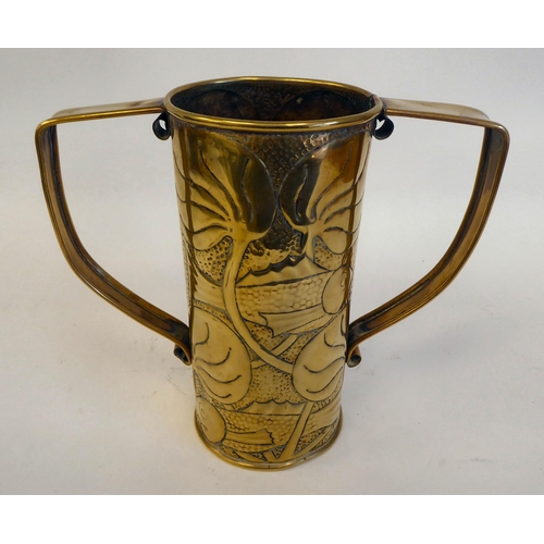 194 - An Arts and Crafts brass vase of cylindrical form with opposing strap handles, embossed with stylise... 