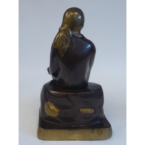 27 - A cast, patinated and part gilded bronze Asian figure, wearing traditional costume and seated on a r... 