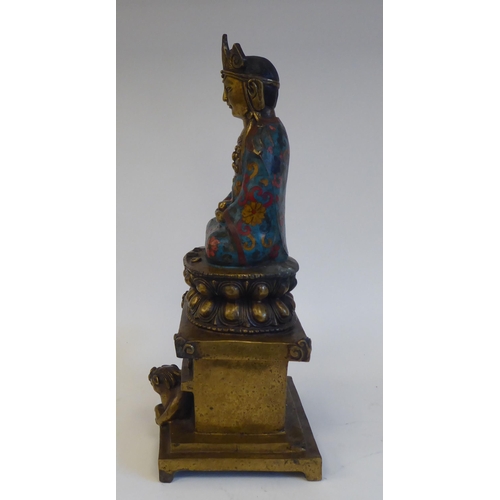 28 - An Asian cast brass and cloisonné Buddhist figure, seated cross-legged on a cushion plinth, g... 