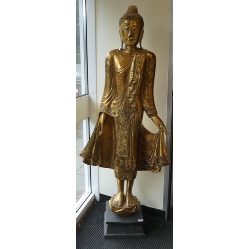 29 - A Burmese carved and gilded teak, standing temple Buddha, holding a myrobalan fruit, on a lotus flow... 