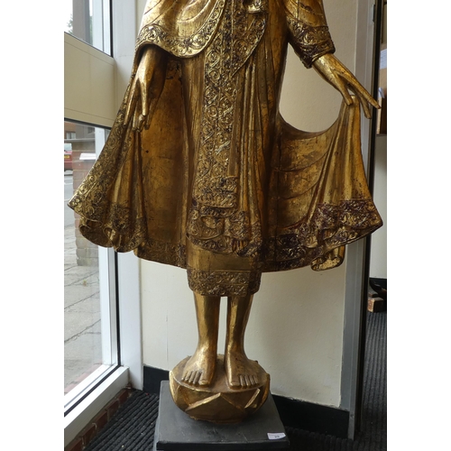 29 - A Burmese carved and gilded teak, standing temple Buddha, holding a myrobalan fruit, on a lotus flow... 