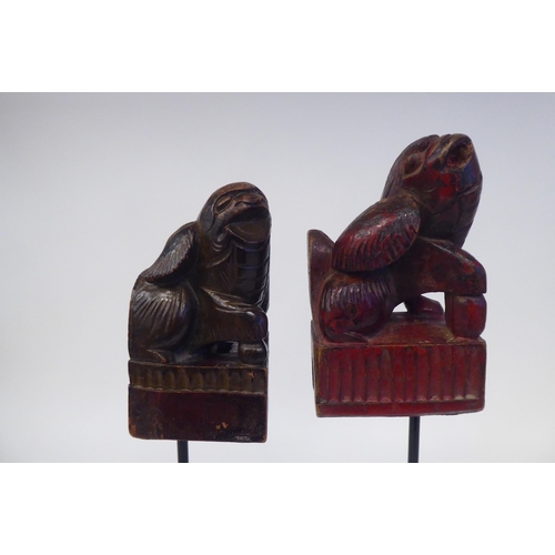 77 - A pair of 20thC Oriental, carved and stained ornaments, in the manner of Dogs of Fo, on a spiked ste... 