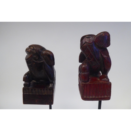 77 - A pair of 20thC Oriental, carved and stained ornaments, in the manner of Dogs of Fo, on a spiked ste... 