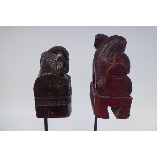 77 - A pair of 20thC Oriental, carved and stained ornaments, in the manner of Dogs of Fo, on a spiked ste... 