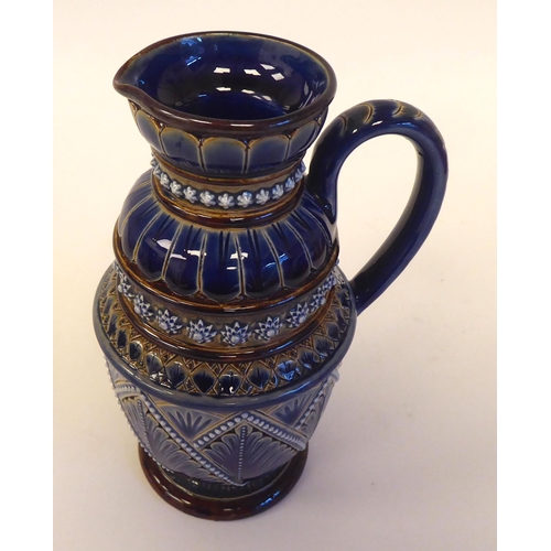 88 - A Doulton Lambeth blue and brown stoneware pedestal jug with a loop handle and cup lip, decorated in... 