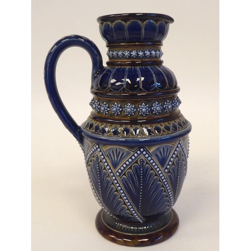 88 - A Doulton Lambeth blue and brown stoneware pedestal jug with a loop handle and cup lip, decorated in... 