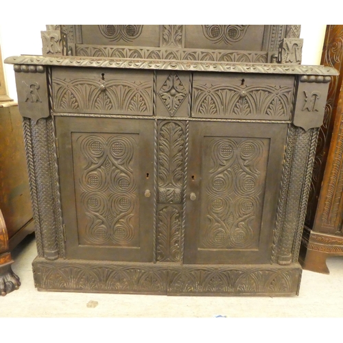 111 - A late 19thC stained and profusely carved, two part cupboard with a canopied superstructure, over a ... 