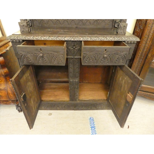 111 - A late 19thC stained and profusely carved, two part cupboard with a canopied superstructure, over a ... 