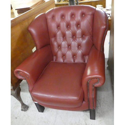 305 - A modern traditional style enclosed armchair, stud and button upholstered in red hide, raised on squ... 