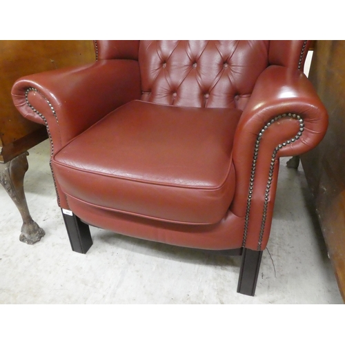 305 - A modern traditional style enclosed armchair, stud and button upholstered in red hide, raised on squ... 