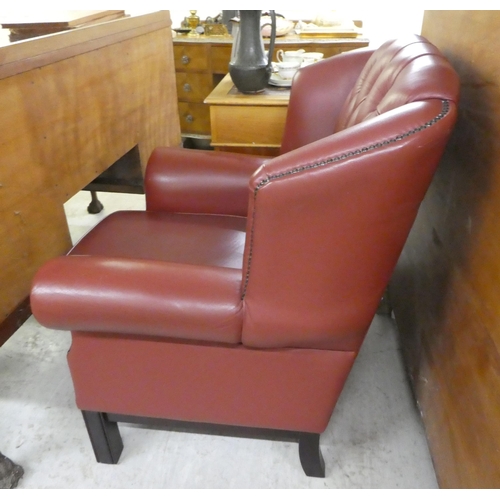 305 - A modern traditional style enclosed armchair, stud and button upholstered in red hide, raised on squ... 