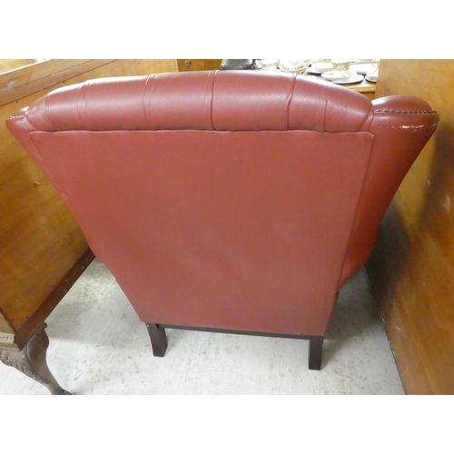 305 - A modern traditional style enclosed armchair, stud and button upholstered in red hide, raised on squ... 