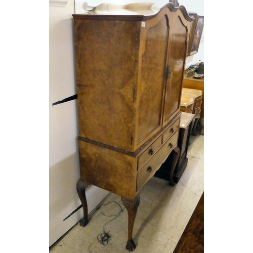 310 - A 20thC quarter veneered walnut two-part cabinet cocktail with a pair of shaped panelled doors, over... 