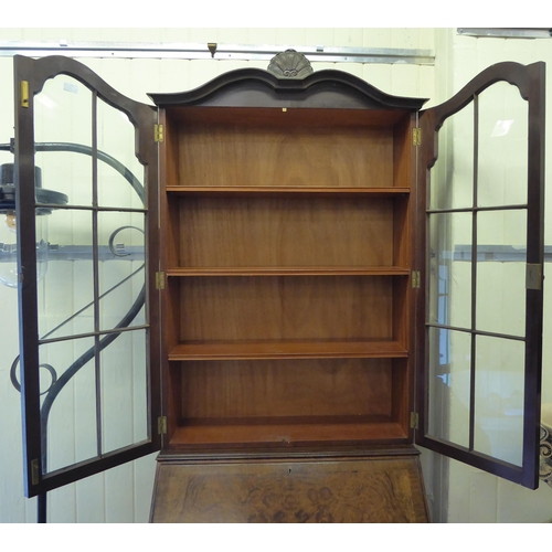 319 - A 20thC crossbanded, walnut veneered bureau bookcase, the upper section with a pair of glazed doors ... 