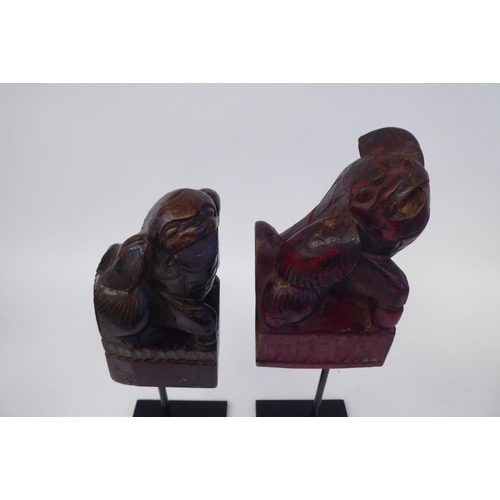 344 - A pair of 20thC Oriental, carved and stained ornaments, in the manner of Dogs of Fo, on a spiked ste... 