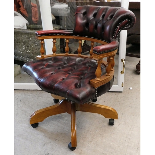 53 - A modern stained beech framed swivel office chair, upholstered in faux maroon hide, on casters