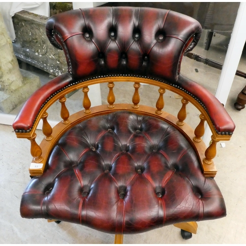 53 - A modern stained beech framed swivel office chair, upholstered in faux maroon hide, on casters